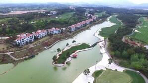 A golf course with a water feature, a bridge, and a row of white buildings with red roofs. - PineRidge Resort (Goseong)
