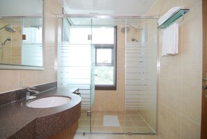 Une salle de bain dotée d’un lavabo avec un plan de toilette en granit, d’une douche à parois de verre et d’une fenêtre laissant entrer la lumière naturelle.