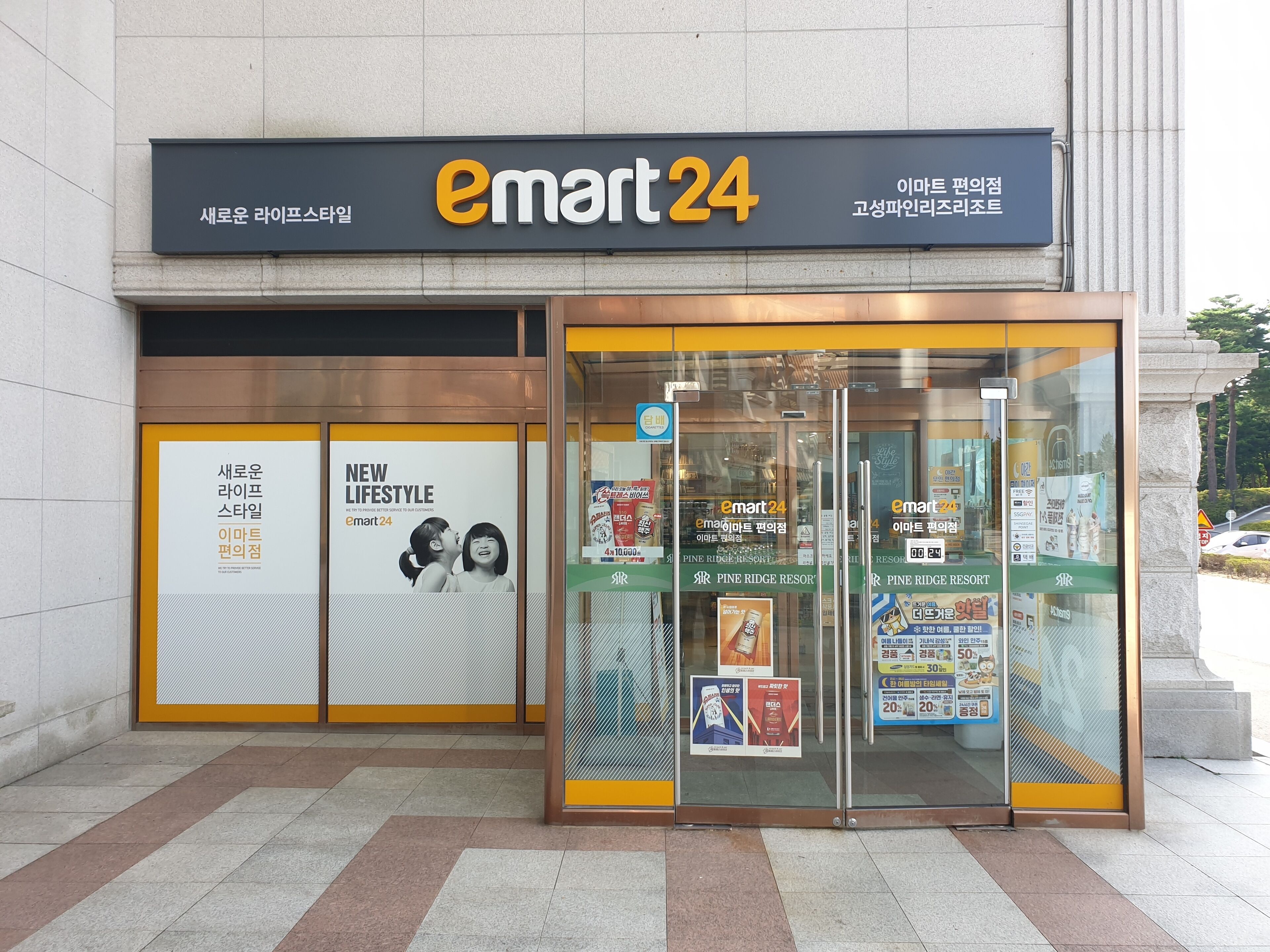 Un escaparate con un letrero grande que dice "emart 24" y una puerta de vidrio de acceso.