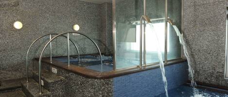 A hot tub with a glass enclosure, metal steps, and a water fountain.