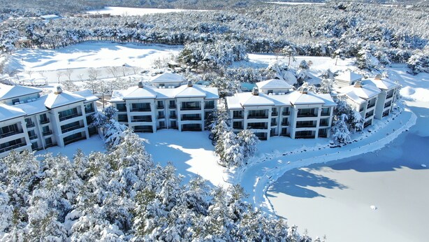 A snow-covered resort with multiple buildings, a lake, and surrounding trees. - PineRidge Resort (Goseong)