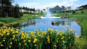 A golf course with a pond, yellow flowers, and a building in the background. - PineRidge Resort (Goseong)