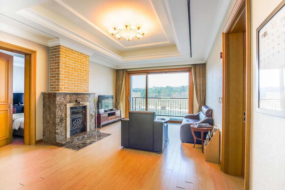 A spacious living room with a fireplace, a balcony with a view, and a cozy seating area.