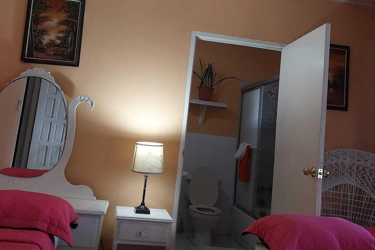 A bedroom with a bed, a nightstand with a lamp, a mirror, and a door leading to a bathroom.