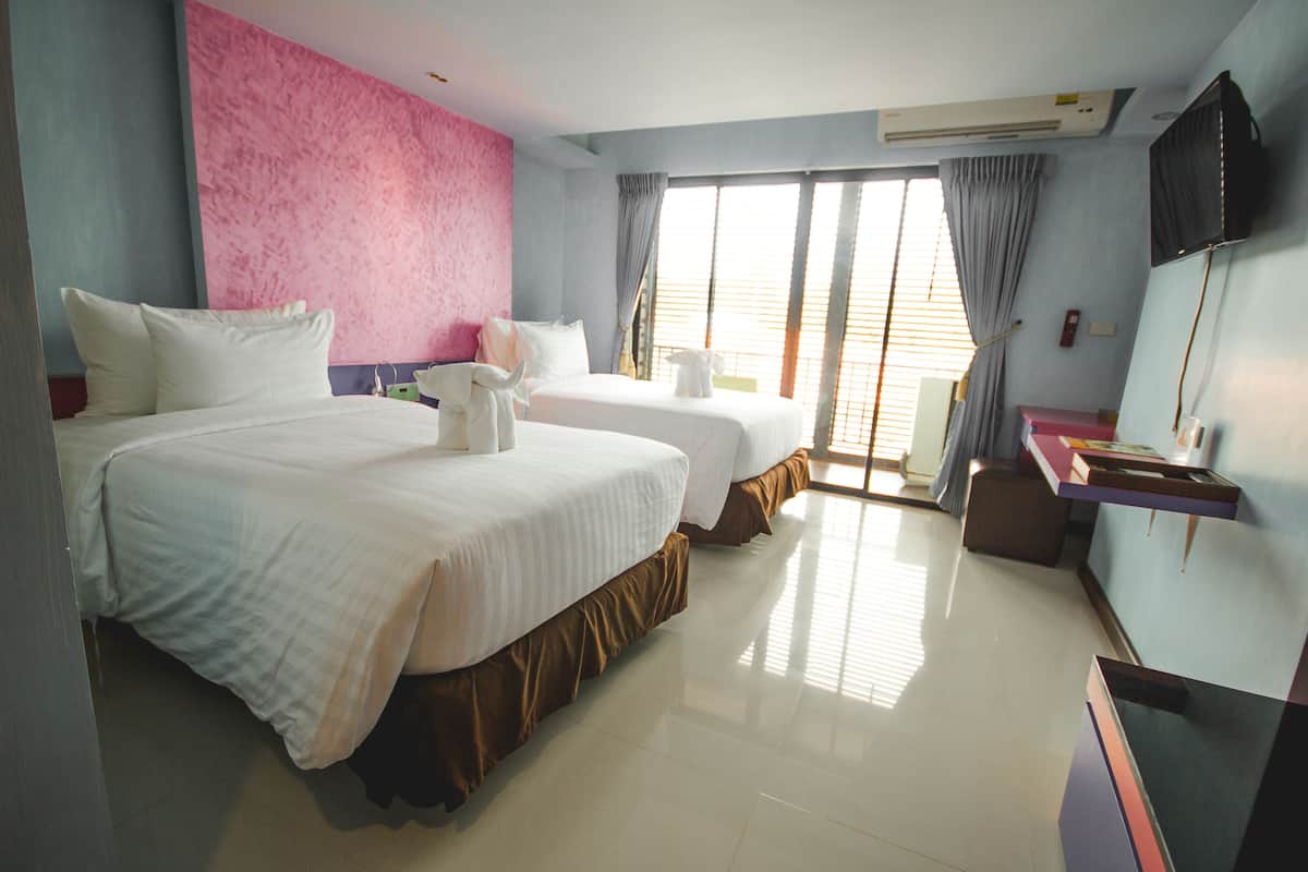 A hotel room with two beds, a desk, a TV, and a large window with curtains.