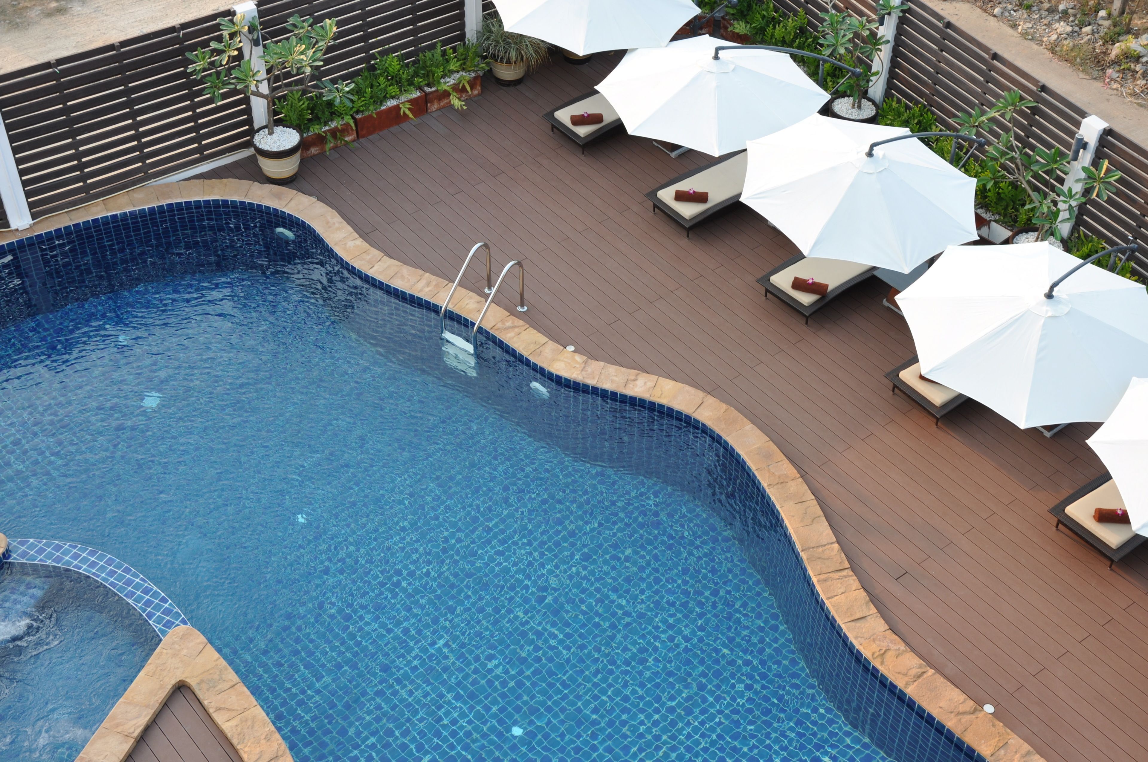 A swimming pool with a tiled edge, surrounded by lounge chairs and umbrellas, and a wooden deck.