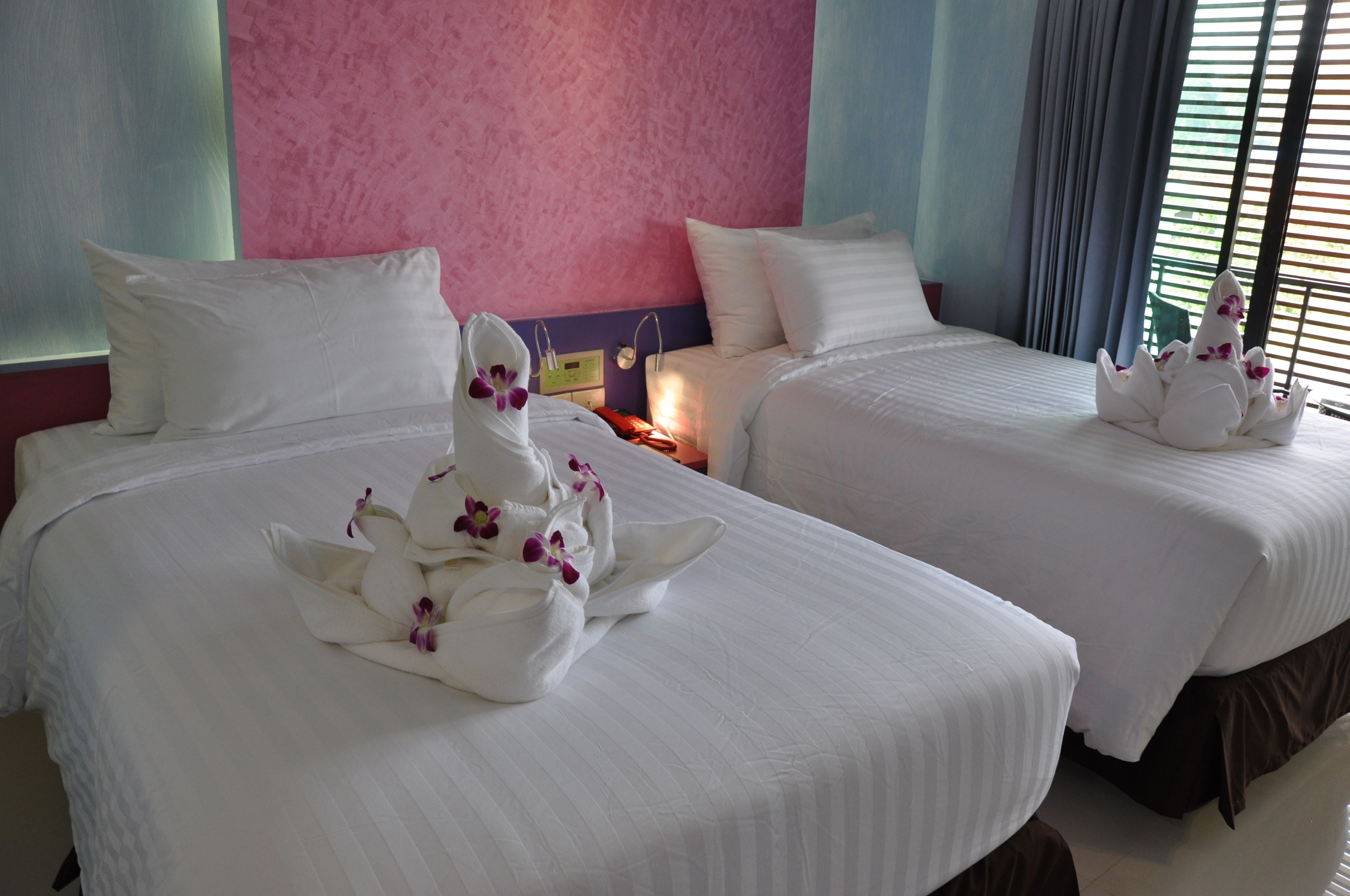 Quarto de hotel com duas camas, cada uma com roupa de cama branca e cisnes decorativos com flores roxas.