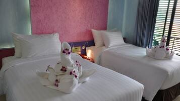 Quarto de hotel com duas camas, cada uma com roupa de cama branca e cisnes decorativos com flores roxas.