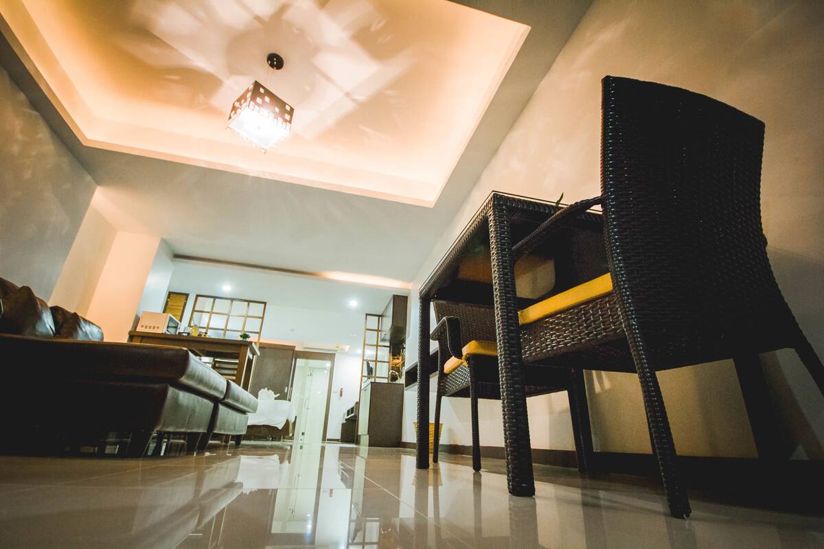 A modern living room with a sofa, a black wicker chair, and a ceiling light fixture.