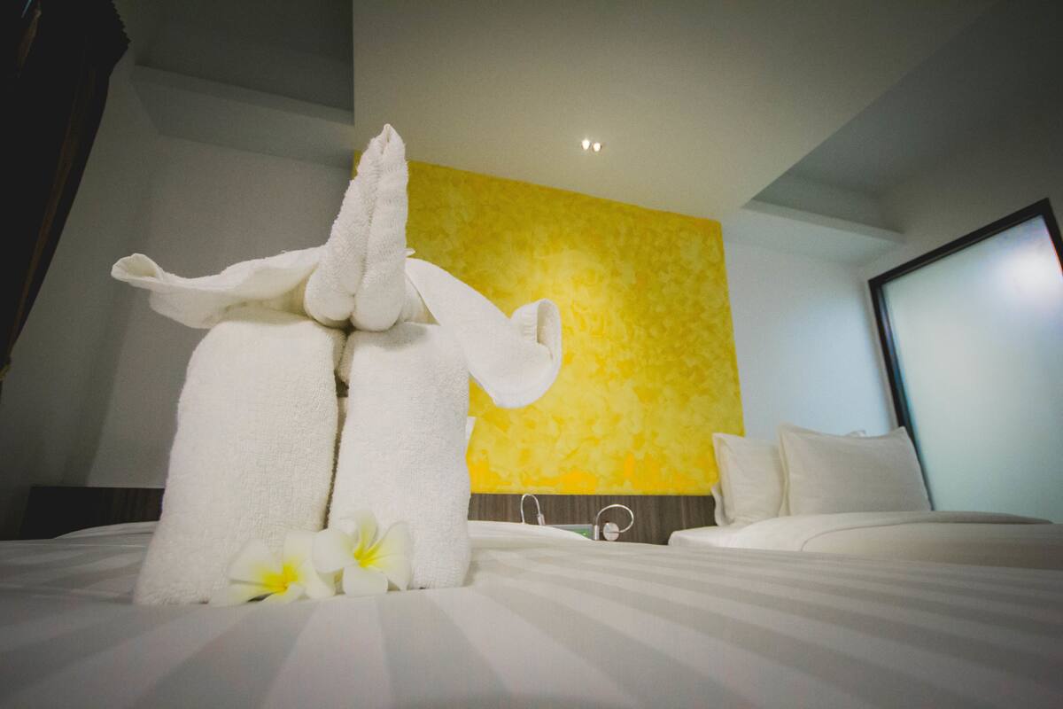 A hotel room with a bed, a large towel sculpture, and a yellow textured wall.