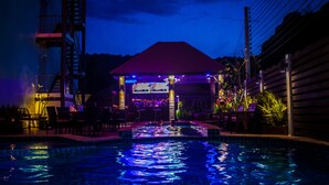 A nighttime swimming pool area with a covered seating area and a bar.
