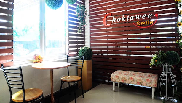 A cozy corner with a wooden slatted wall, a round table, two chairs, a bench, and a decorative vase. - Choktawee Smile (Chiang Mai)