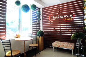 A cozy corner with a wooden slatted wall, a round table, two chairs, a bench, and a decorative vase. - Choktawee Smile (Chiang Mai)