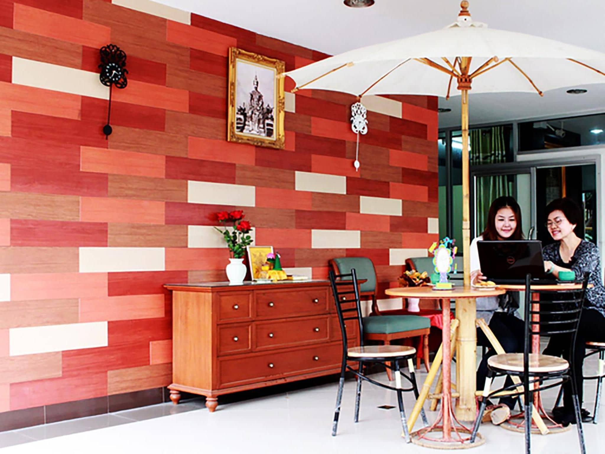 A dining area with a red and white patterned wall, a wooden cabinet, a table with chairs, and a large umbrella.