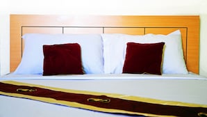 A bed with white and red pillows, a wooden headboard, and a bedspread with a gold emblem. - Choktawee Smile (Chiang Mai)