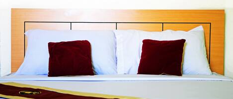 A bed with white and red pillows, a wooden headboard, and a bedspread with a gold emblem.