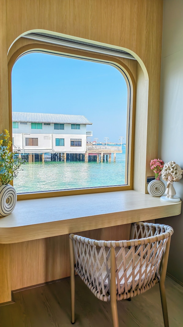 A wooden desk with a large window overlooking a waterfront building. - Moonlight Koh Larn (Koh Lan)