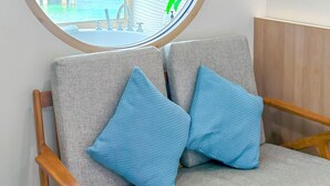 A room with a round window, a grey sofa with blue cushions, and a wooden chair. - Moonlight Koh Larn (Koh Lan)
