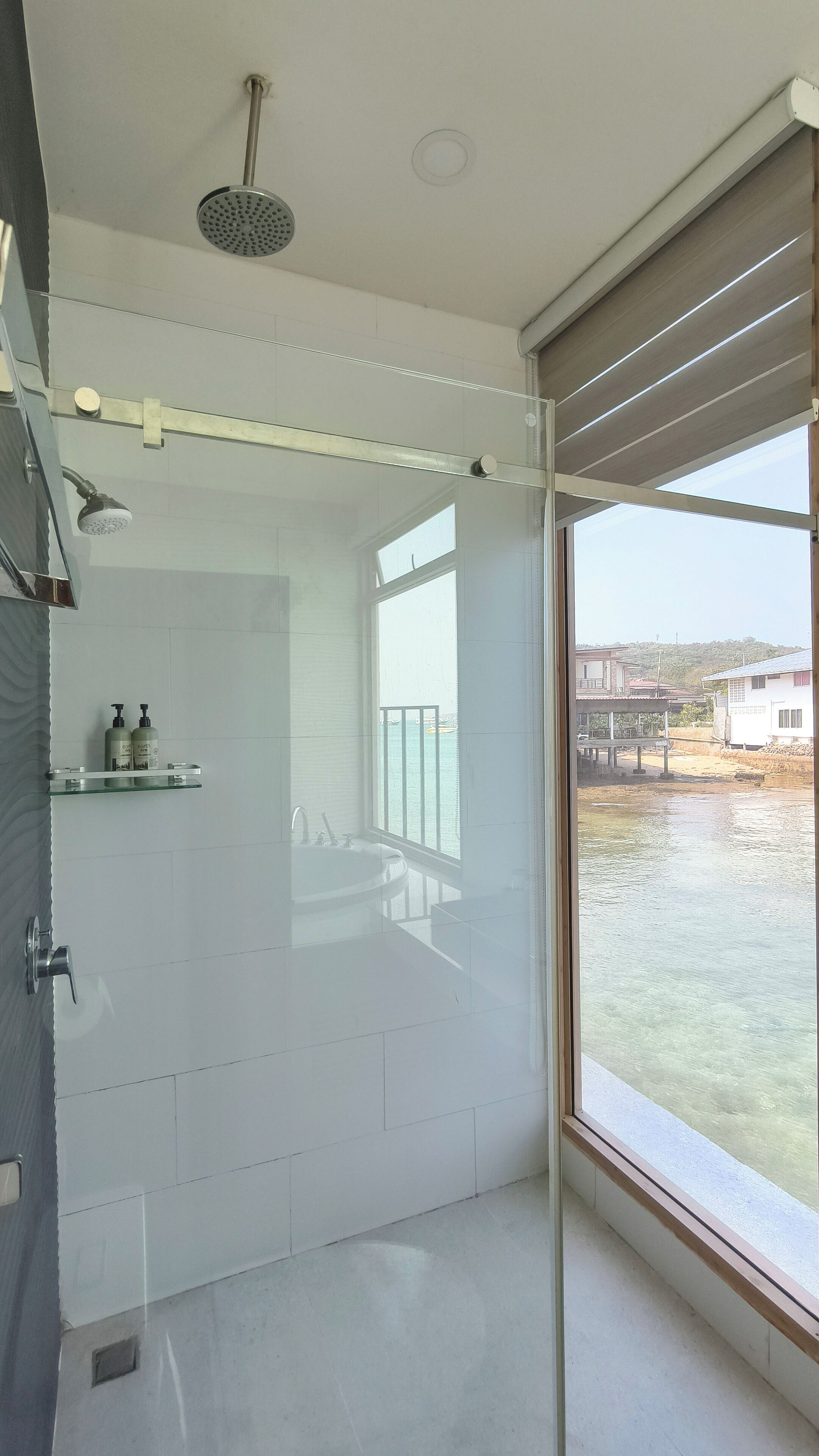 Un bagno moderno con cabina doccia in vetro, un'ampia finestra vista mare e un piccolo ripiano con articoli da toilette.