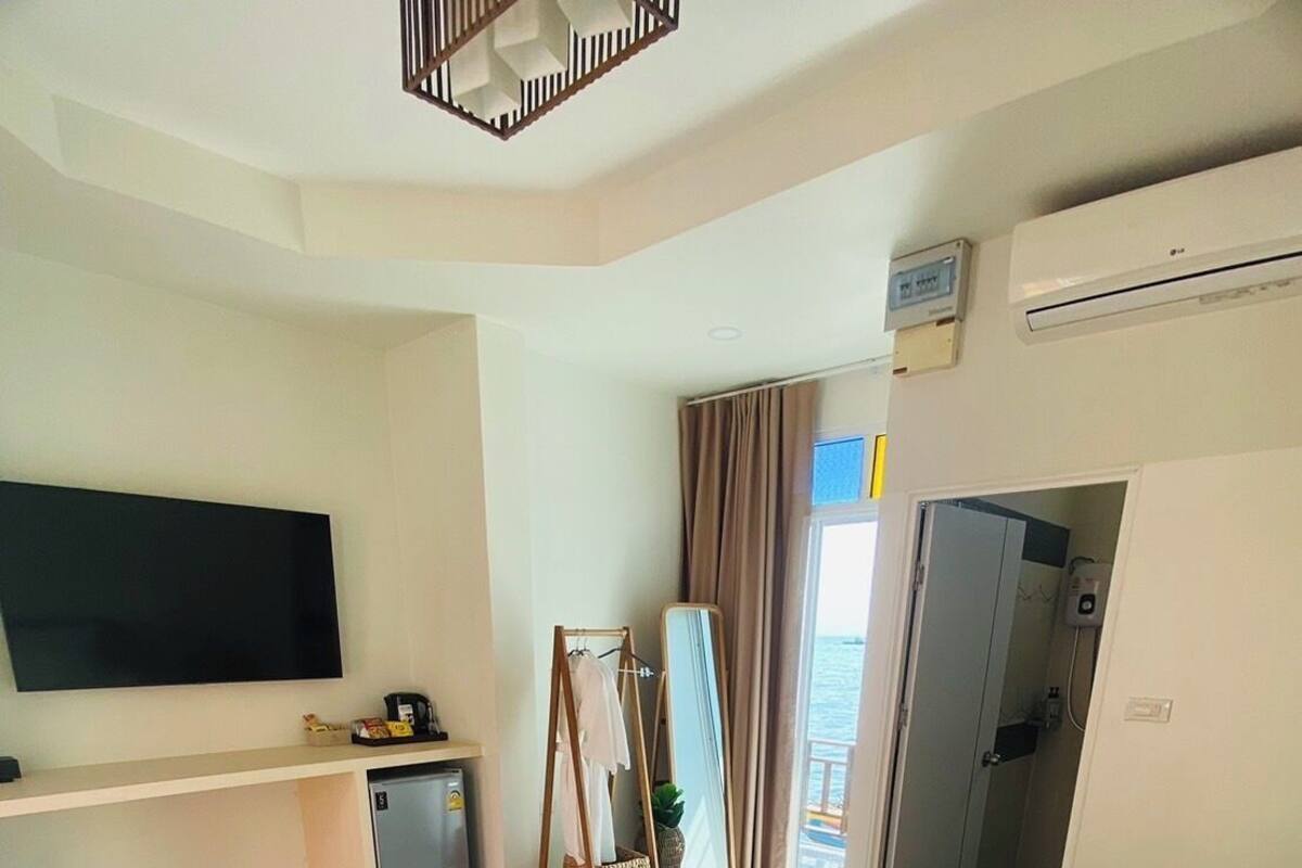 A hotel room with a bed, a TV, a desk, a mirror, and a shower area.