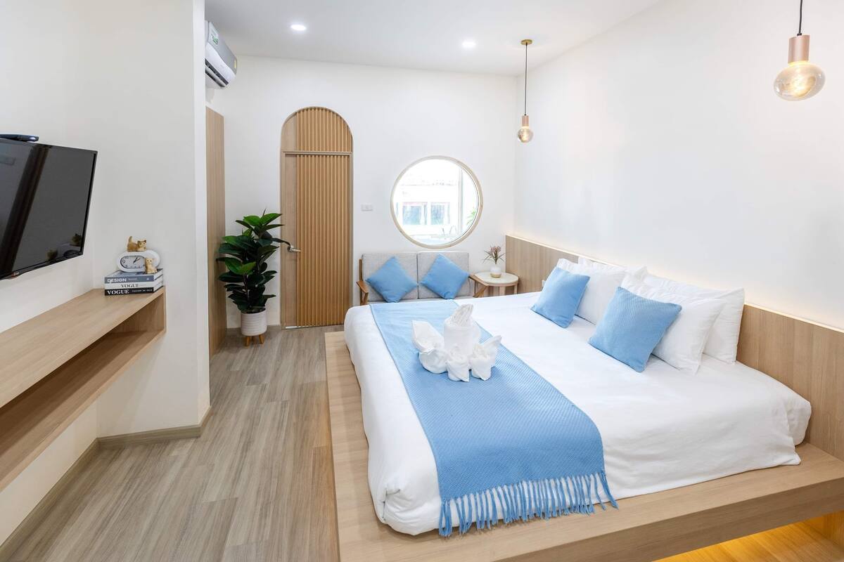 A modern hotel room with a large bed, a TV, a round mirror, and a wooden door.