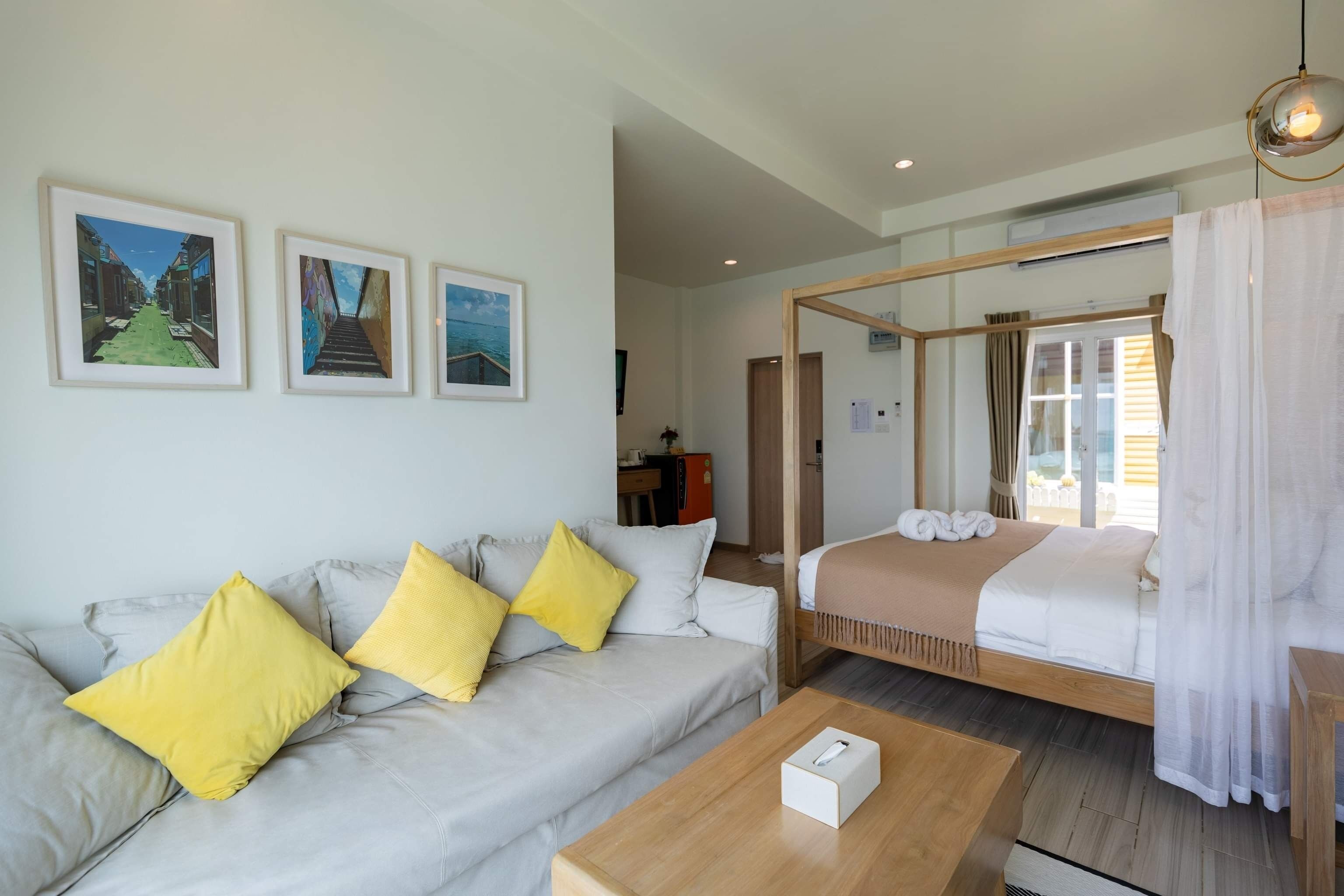 A hotel room with a bed, a sofa with yellow pillows, a coffee table, and framed pictures on the wall.