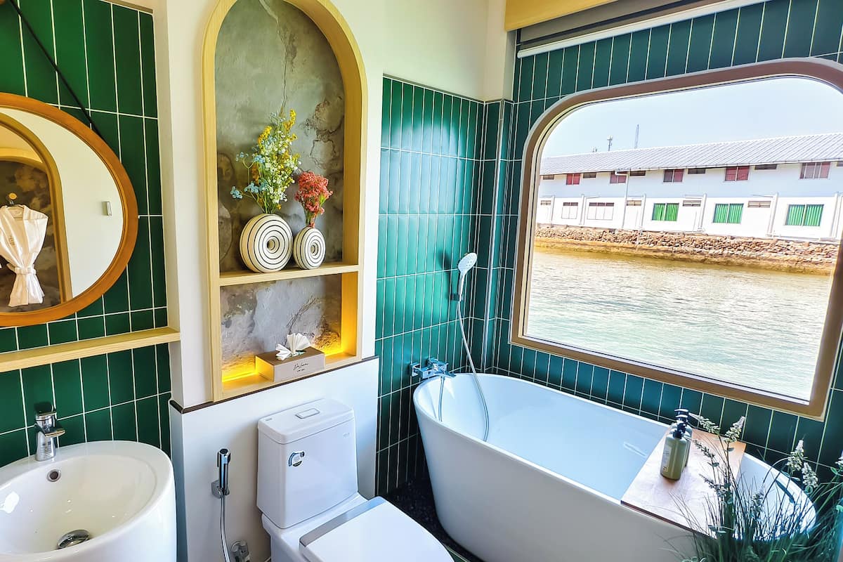 A bathroom with a bathtub, sink, and mirror. There is a window with a view of a building and a body of water.