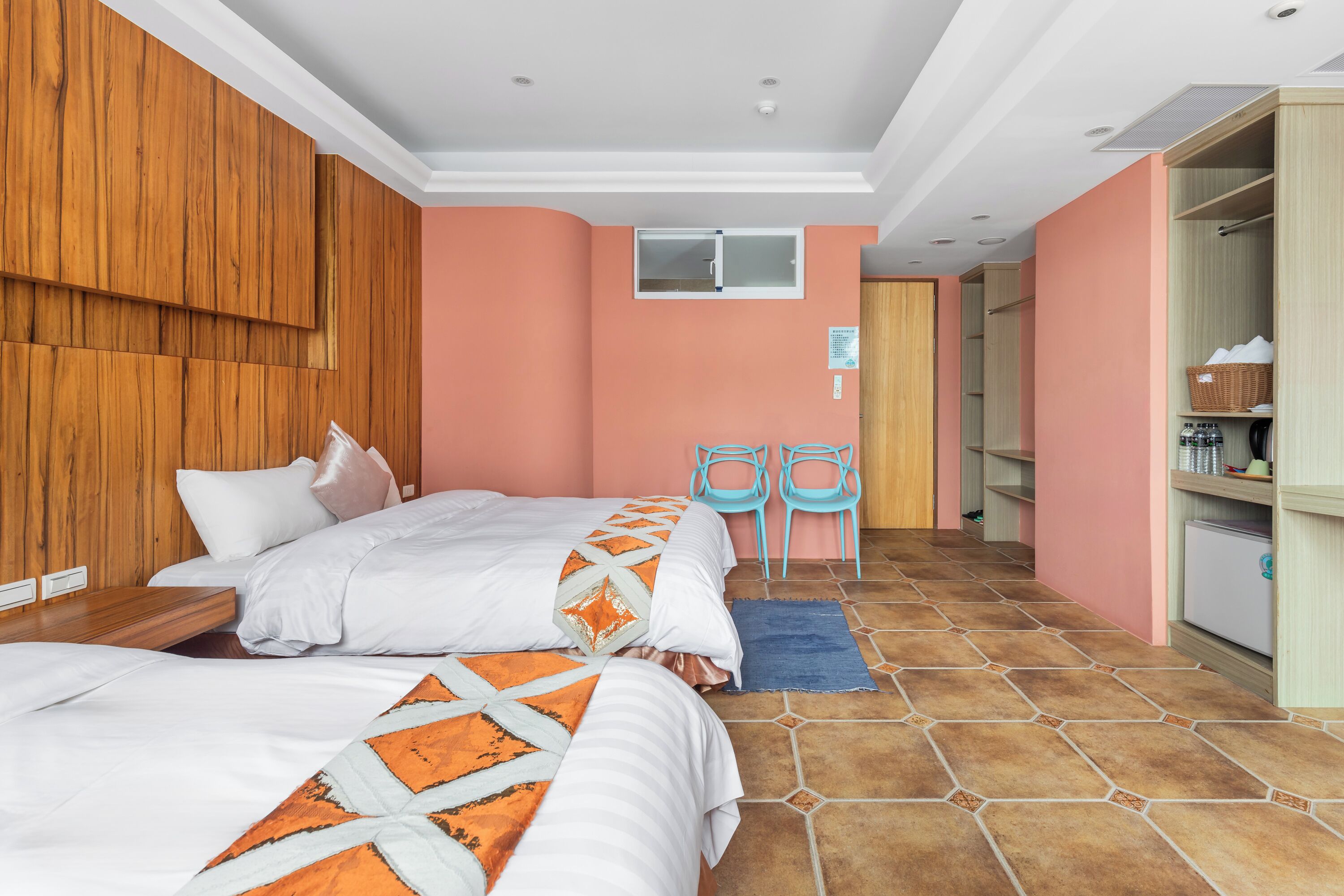 Une chambre d’hôtel avec deux lits, une armoire en bois, une petite fenêtre et un coin cuisine.