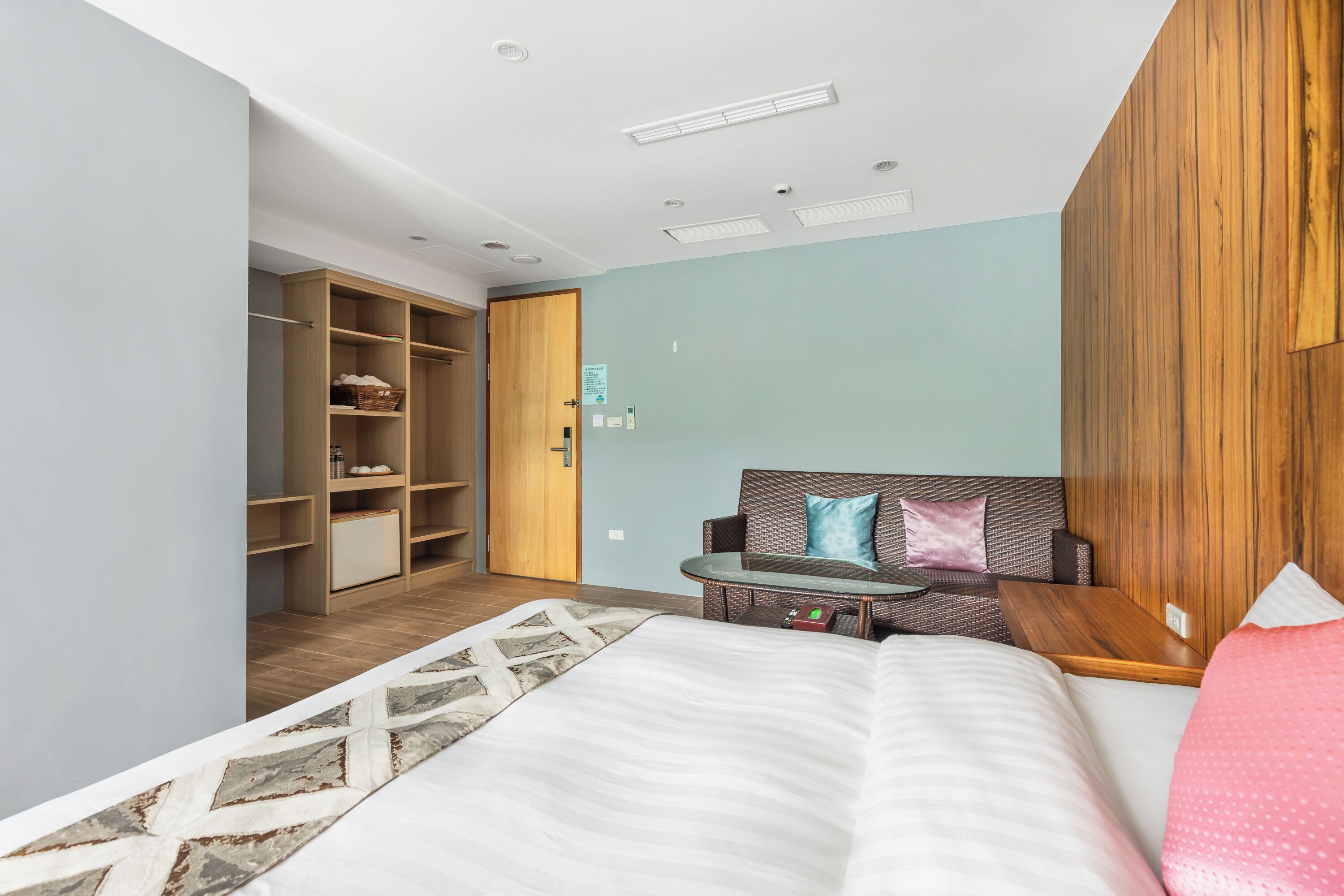 Quarto de hotel moderno com cama, área de estar com mesa, guarda-roupa e porta que dá para outro quarto.