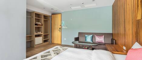 Quarto de hotel moderno com cama, área de estar com mesa, guarda-roupa e porta que dá para outro quarto.