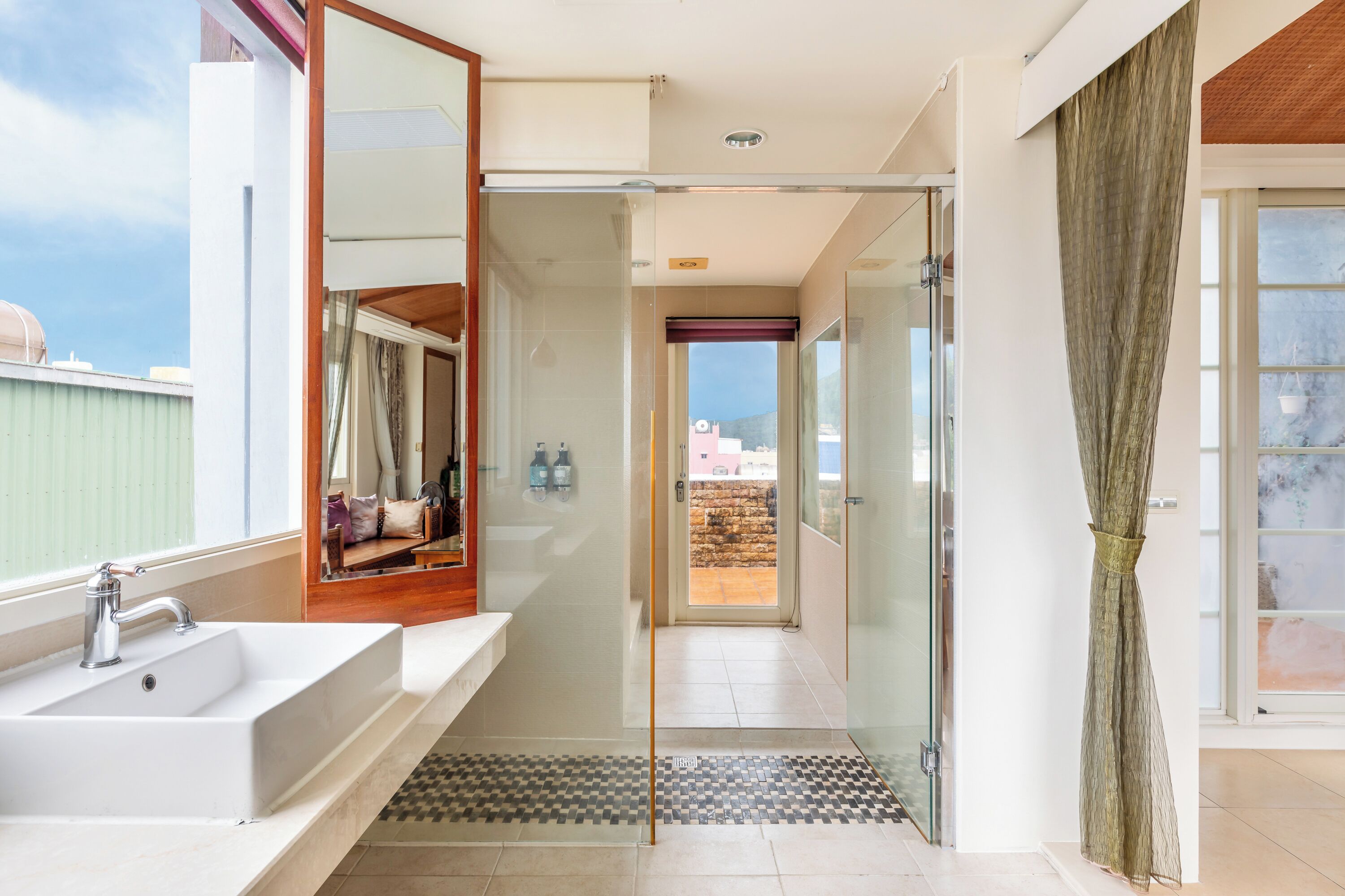 Een moderne badkamer met een douchecabine van glas, een groot wastafelmeubel en uitzicht op buiten.