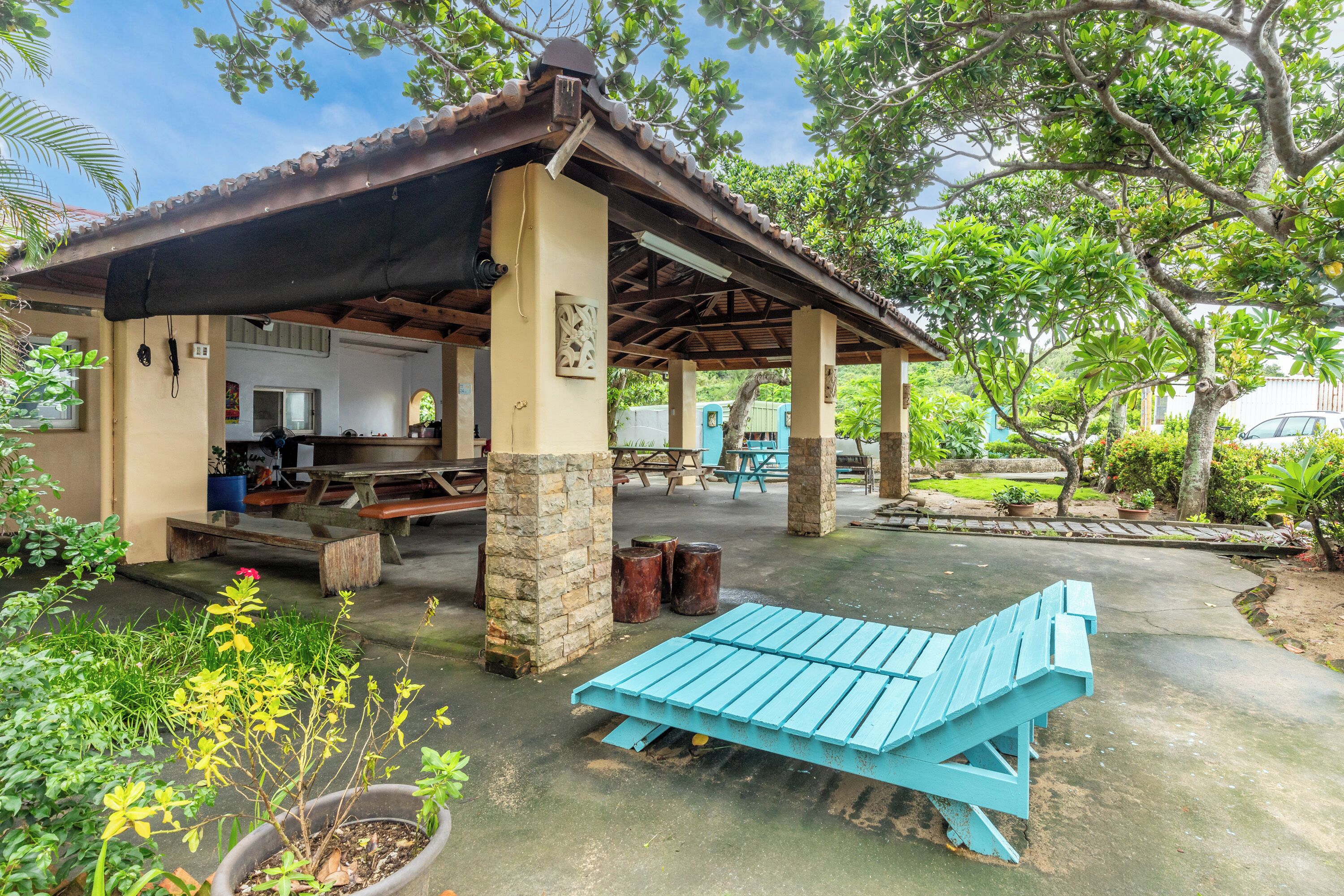 A covered outdoor seating area with a blue bench, stone pillars, and potted plants.