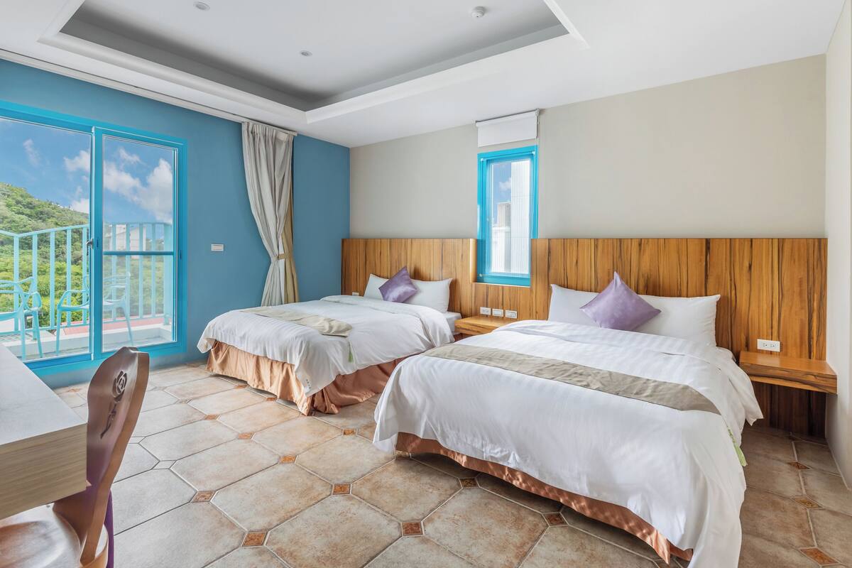 A hotel room with two beds, a wooden headboard, a window with a view, and a balcony.