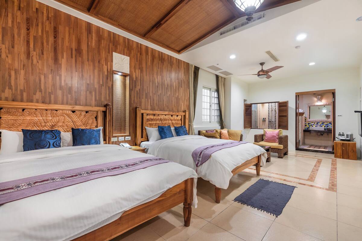 A hotel room with two wooden beds, a ceiling fan, and a bathroom visible through an open door.