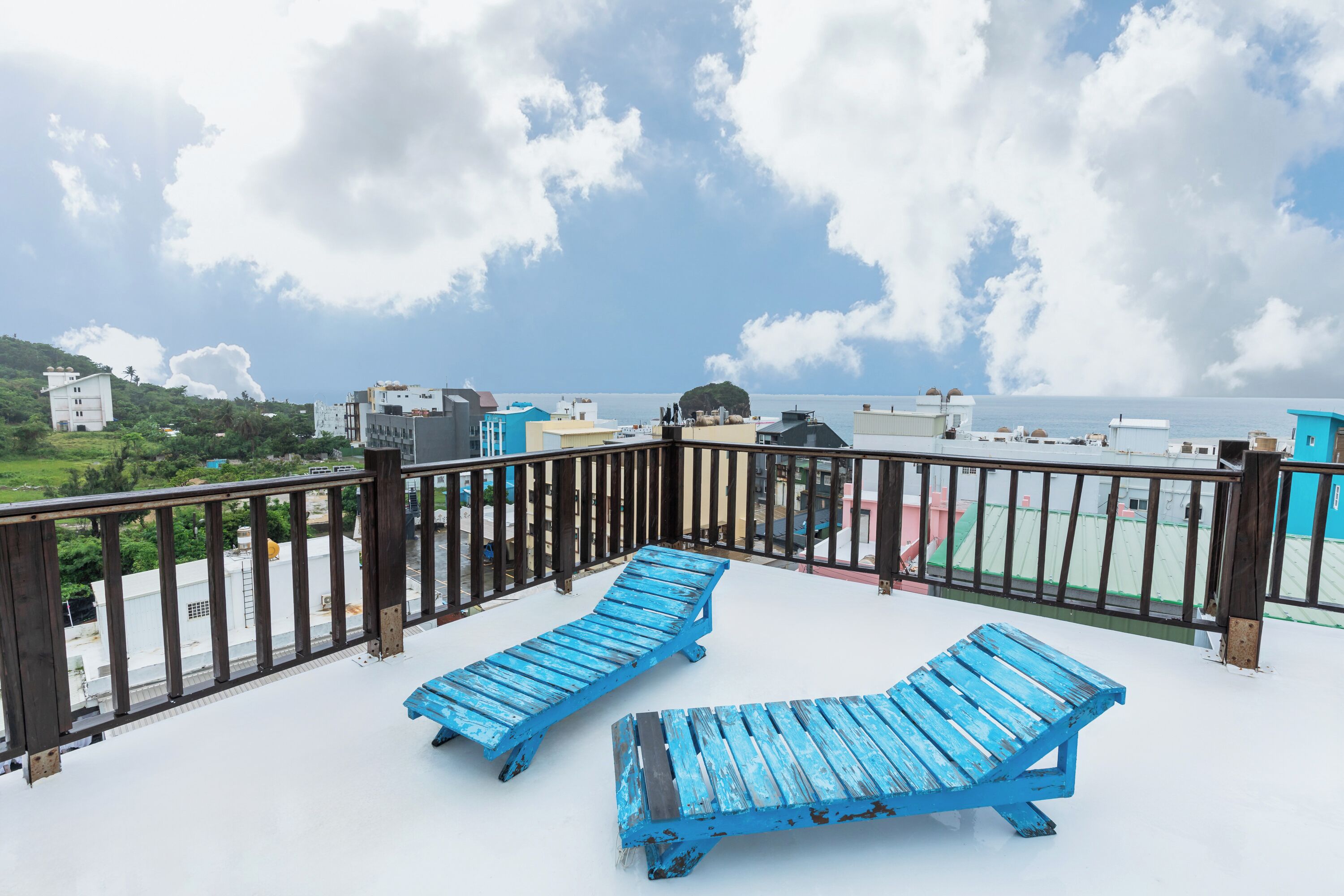 A rooftop terrace with two blue lounge chairs and a wooden railing.