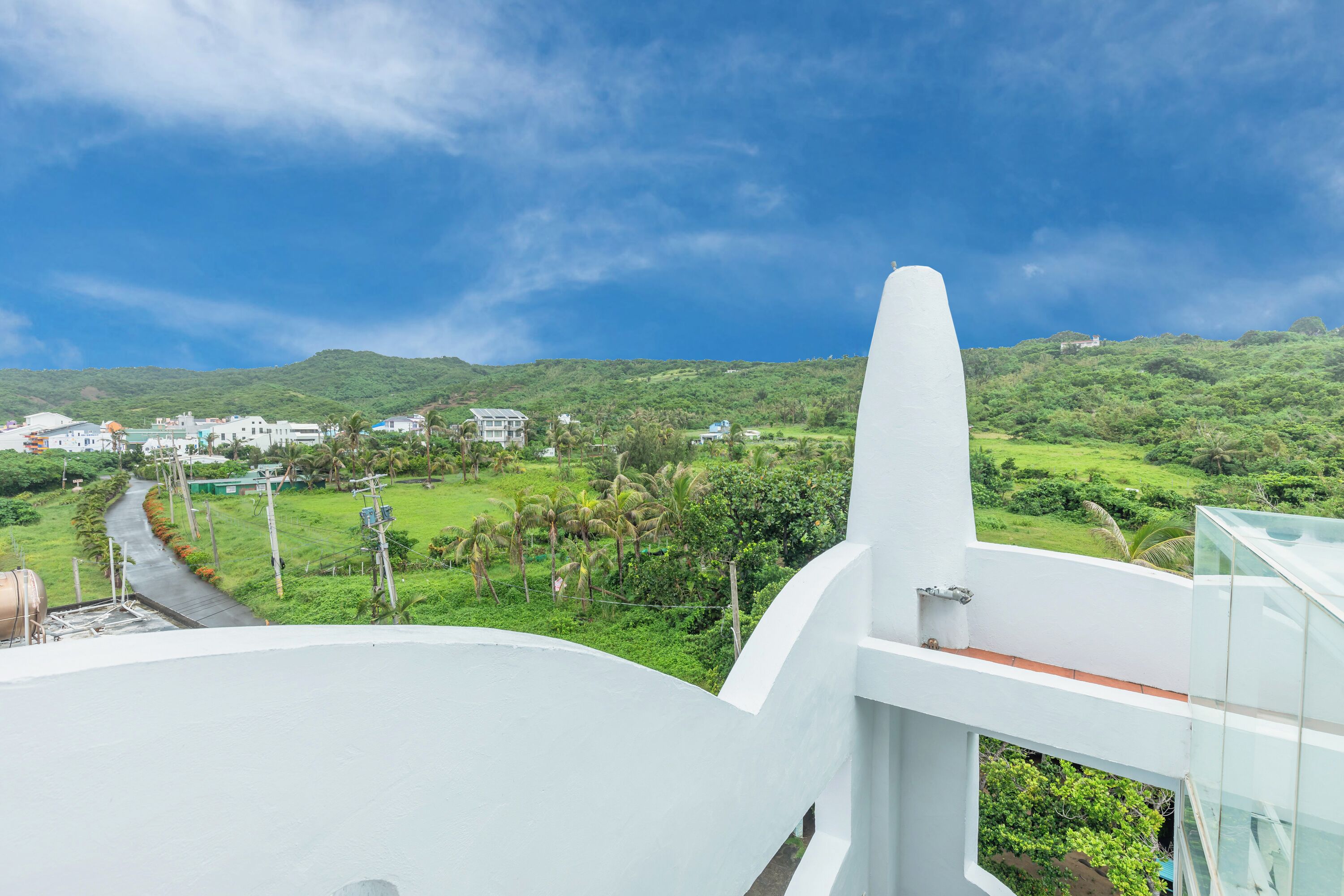 A modern building with a curved roof, overlooking a lush green landscape with hills and a clear sky.