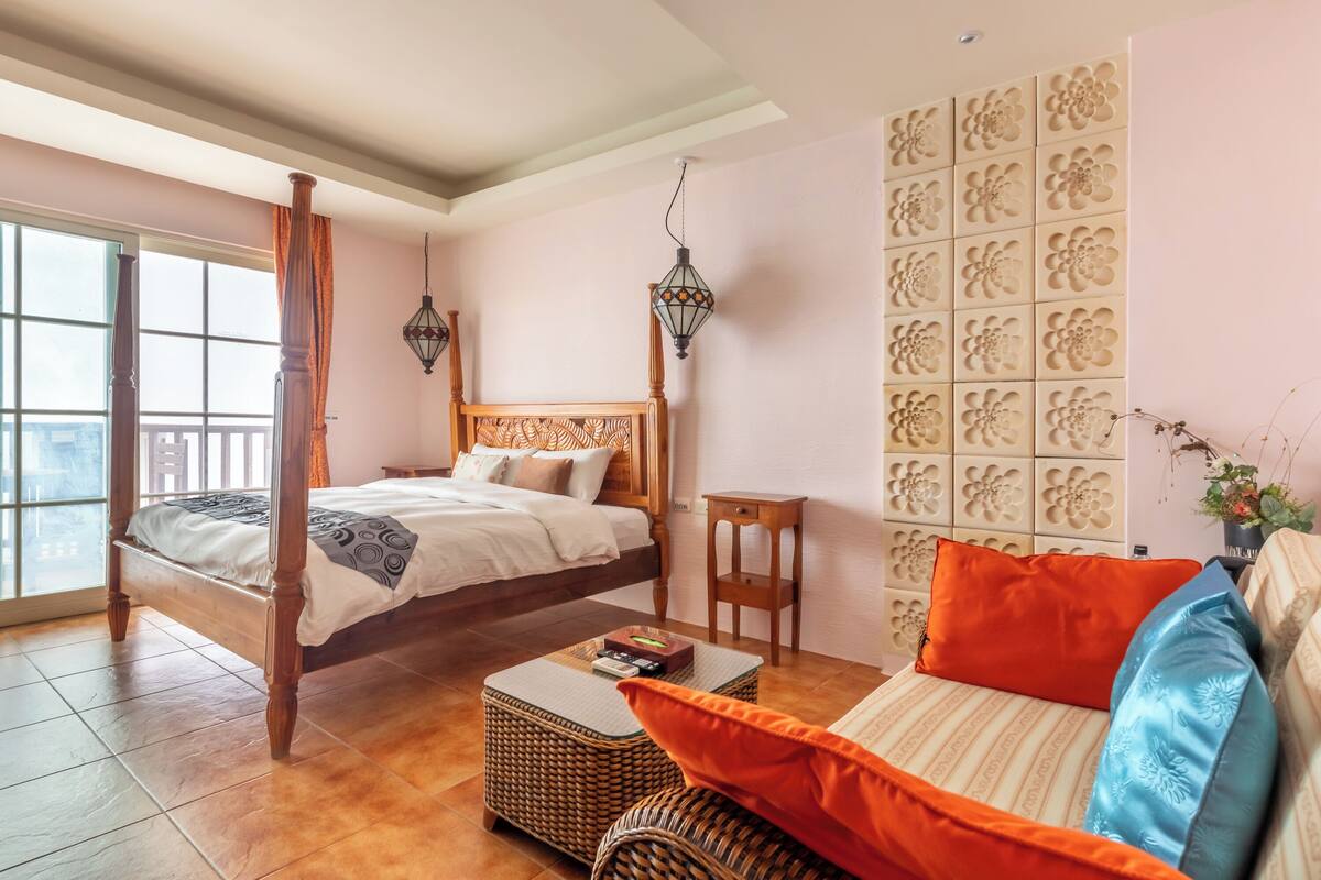 A bedroom with a large bed, a small table, a sofa, and a decorative wall.