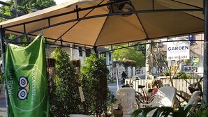 An outdoor seating area with a canopy, white plastic chairs, potted plants, and a sign for 'Garden Wedding'. - Chiangmai Gate Capsule Hostel (Chiang Mai)