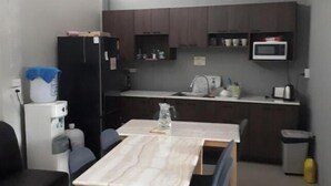 A compact living space with a dining table, two chairs, a black sofa, a kitchen area with a microwave, and a water dispenser. - Chiangmai Gate Capsule Hostel (Chiang Mai)