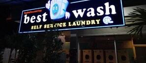A sign for a self-service laundry facility with a cartoon character and 24-hour service.