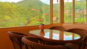 A dining area with a round glass table and wicker chairs, overlooking a mountainous landscape with buildings. - Formosa Arcadian Villa (New Taipei City)