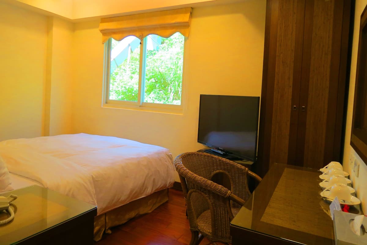 Een hotelkamer met een bed, een televisie, een rieten stoel en een houten garderobe.