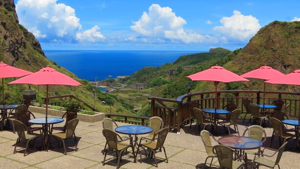An outdoor seating area with tables and chairs, overlooking a coastal landscape with a view of the sea and hills. - Formosa Arcadian Villa (New Taipei City)