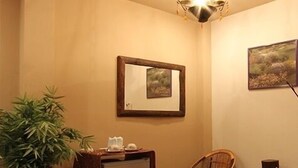 A room with a wooden cabinet, a small table with a plant, a chair, a framed picture on the wall, and a ceiling light fixture. - ThongRan's house (Chiang Mai)