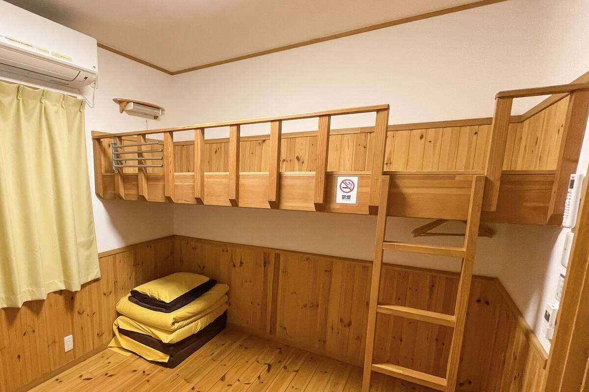 A bunk bed room with a wooden floor, a green curtain, and an air conditioning unit.