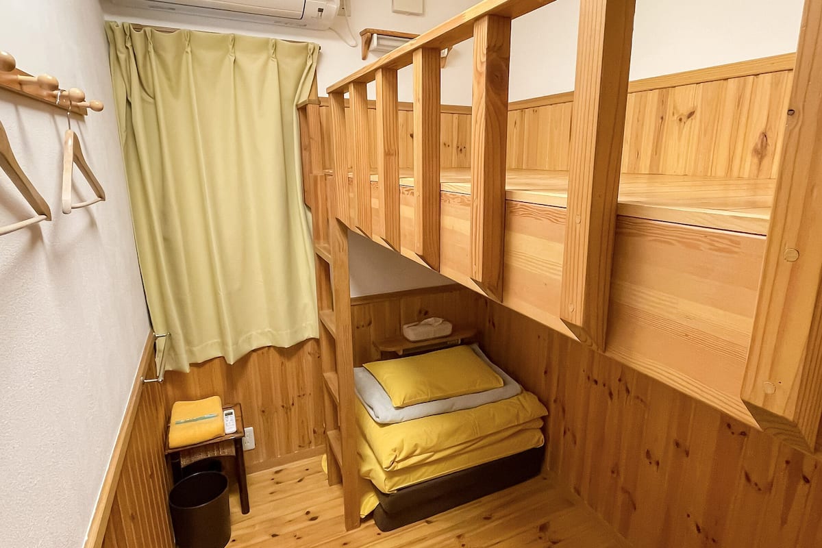 A compact room with a bunk bed, a small table with a chair, a hanging coat rack, and a curtain.