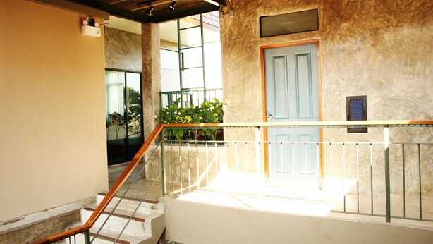 A staircase with a wooden handrail leading to a landing with a blue door and a small window. - Plern Plern Bed and Bike (Chiang Mai)