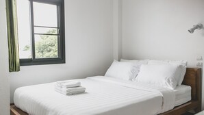 A neatly made bed with white linens and a wooden headboard, a window with a view of greenery, and a wall-mounted light fixture. - Plern Plern Bed and Bike (Chiang Mai)