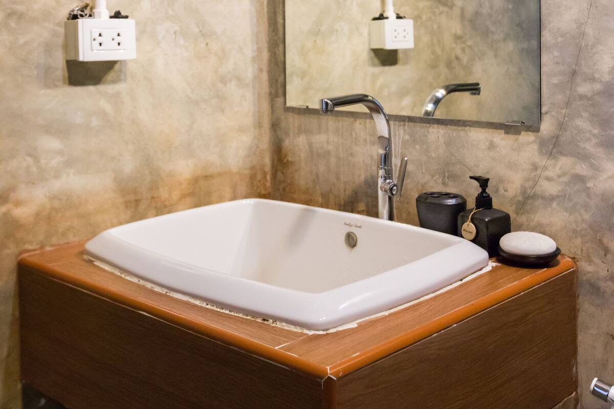 Une salle de bain avec un mur en marbre, un meuble-lavabo en bois, un lavabo blanc, un miroir et un porte-serviettes.