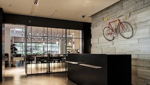 Un'area reception moderna con parete in legno, una bicicletta appesa al muro e un divisorio in vetro che separa la reception dalla sala da pranzo.